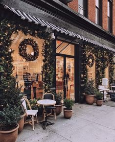 a store front with potted plants and christmas wreaths on the windows, along with chairs and tables