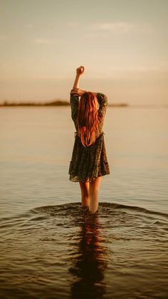 a woman is standing in the water with her arms up and looking at the sky