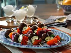 a plate filled with skewered vegetables on top of a wooden table next to glasses