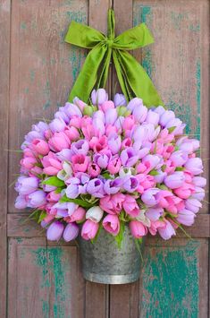 a metal bucket filled with pink and purple tulips next to a green bow