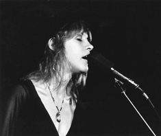 a woman singing into a microphone while standing in front of a black and white photo