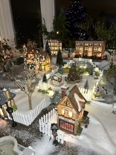 a miniature christmas village with lights and trees in the snow, surrounded by small houses