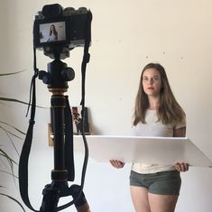 a woman standing in front of a camera holding a piece of paper