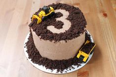 a birthday cake that is on top of a wooden table with construction vehicles around it