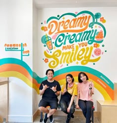 three women sitting on a bench in front of a wall with the words dream creamy make you smile