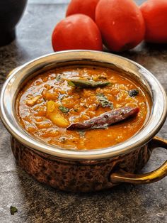 a metal bowl filled with food on top of a counter next to tomatoes and other vegetables