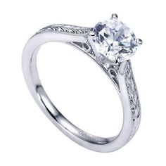 a white gold engagement ring with an engraved design on the band and a round diamond center stone