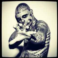 a man with tattoos on his body and face is holding out his hands in front of the camera