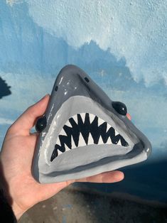 a hand is holding a gray and black shark tooth shaped object in front of a blue painted wall