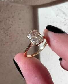 a person holding a ring in their hand with a square shaped diamond on the side