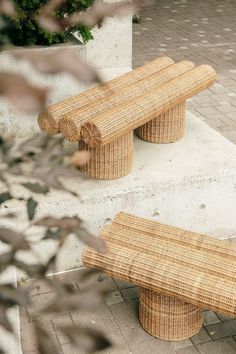 two benches made out of wicker sitting on the side of a sidewalk next to bushes