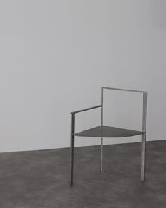 a chair sitting on top of a cement floor next to a white wall with a metal frame