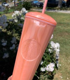 a person holding up a pink starbucks cup in front of some bushes and flowers on the grass