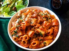 two bowls filled with pasta next to a salad