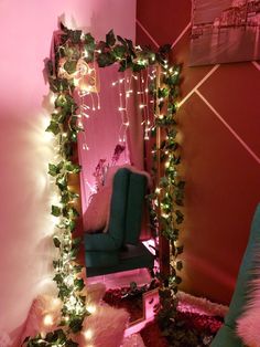 a mirror with christmas lights on it next to a green chair and pink wall in the background