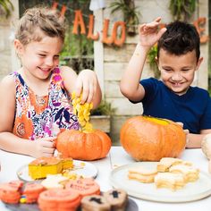 two children sitting at a table with pumpkins and cookies