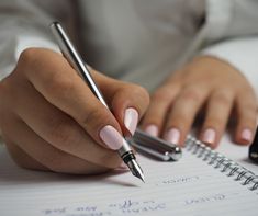 a woman's hand holding a pen and writing on a notebook