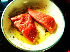 two pieces of fish are in a pan on the stove top with oil and seasoning