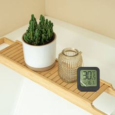 there is a clock on the shelf next to a potted plant in the bathtub