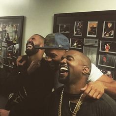 three men laughing together in a room with pictures on the wall