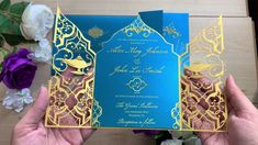 two hands holding up a blue and gold wedding card