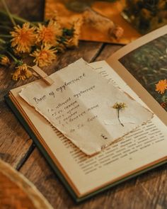 an open book sitting on top of a wooden table next to flowers and papers with writing