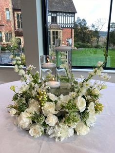 a centerpiece with white flowers and candles on a table in front of a window