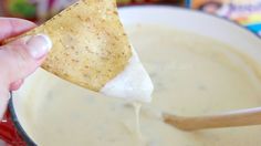 a hand holding a tortilla chip over a bowl of quesadilla dip