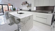 a kitchen with white cabinets and marble counter tops, two bar stools in front of the sink