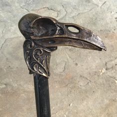 a metal bird head on top of a black pole next to a stone floor and wall