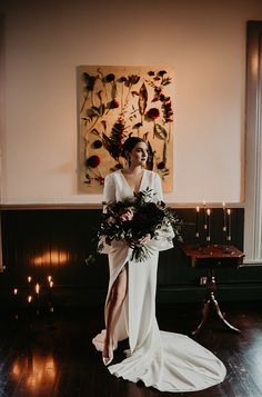 a woman in a white dress holding a bouquet standing on a wooden floor next to a painting