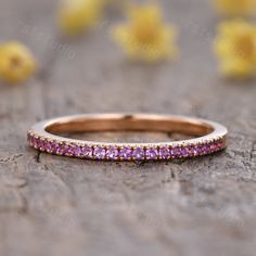 a pink diamond ring sitting on top of a wooden table with yellow flowers in the background