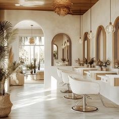 the interior of a hair salon with white chairs and large mirrors on the wall, potted plants in front of them