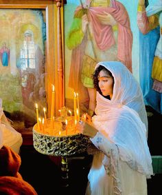 a woman holding a cake with lit candles on it in front of other people and paintings