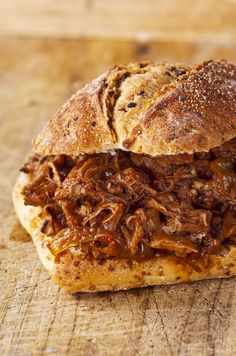 a pulled pork sandwich sitting on top of a wooden cutting board