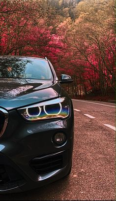 a black car parked on the side of a road next to trees with red leaves