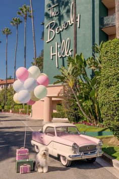 a pink car parked in front of the beverly hills hotel with balloons attached to it