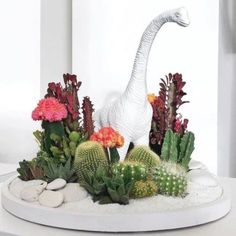 a white dinosaur statue surrounded by succulents and cacti