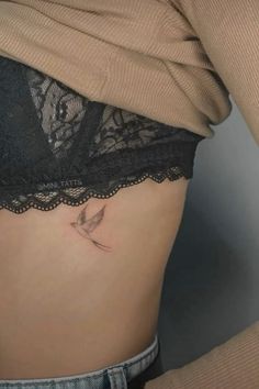 a woman's stomach with a small bird tattoo on the side of her belly