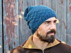 a man with a beard wearing a blue knitted hat against a wooden fence background