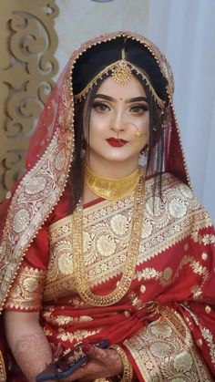 a woman in a red and gold bridal outfit holding a pair of blue scissors