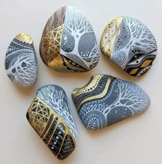 four painted rocks sitting next to each other on a white surface with gold and black designs