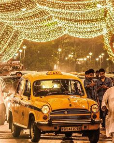 a taxi cab driving down a busy street next to tall buildings covered in christmas lights