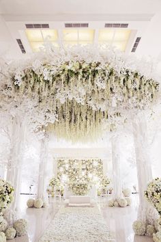 a wedding ceremony with white flowers and greenery on the ceiling, along with an aisle