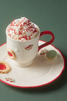 a white cup filled with whipped cream and sprinkles on top of a saucer