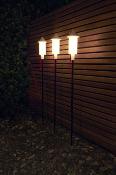 three lights are lit up on the side of a wooden wall in front of some rocks