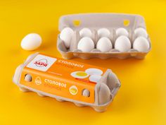 two cartons of eggs sitting next to each other on a yellow surface with an egg in the middle