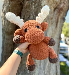 a hand holding a small crocheted stuffed animal in front of a large tree