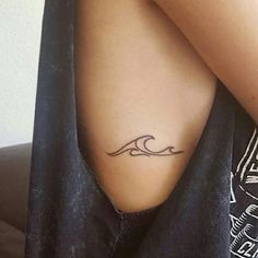 a woman with a small wave tattoo on her left side ribcage is sitting down