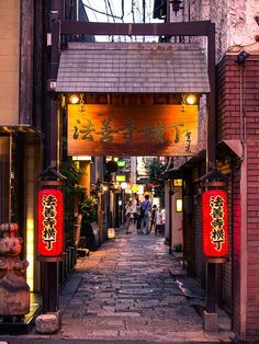 an alley way with lanterns and statues on both sides, surrounded by brick buildings in the background